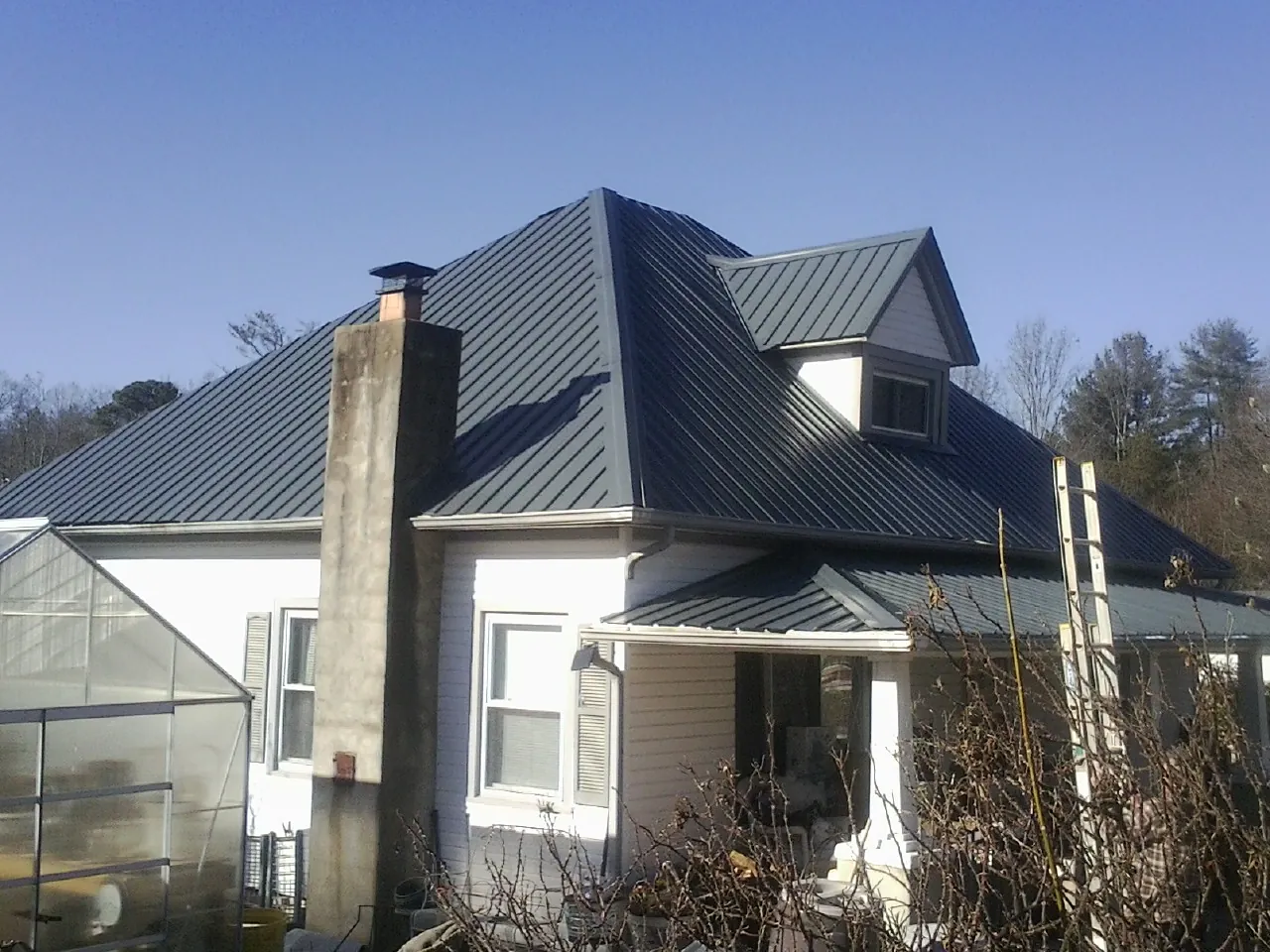Dark blue standing seam metal roof on a white farmhouse with dormer in Watertown